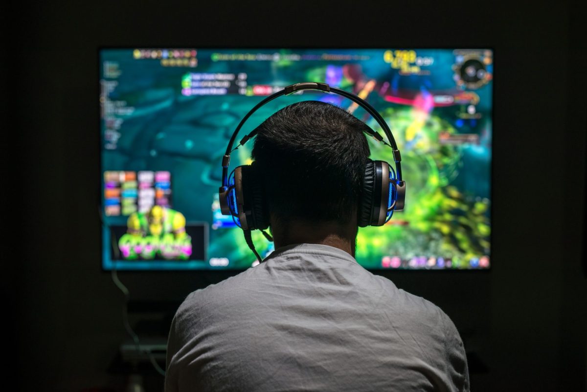 Gamer sitzt mit einem Headset auf dem Kopf vor einem Bildschirm, auf dem eine Spiel läuft.