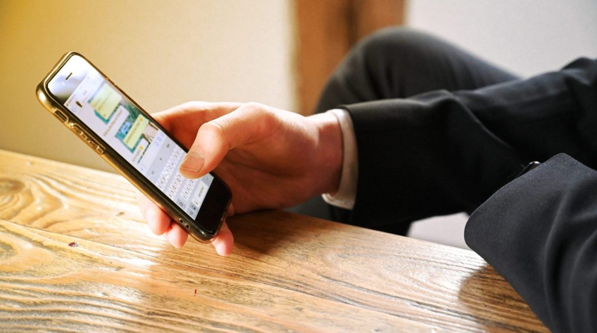 Mann hält Smartphone, auf dem WhatsApp geöffnet ist.