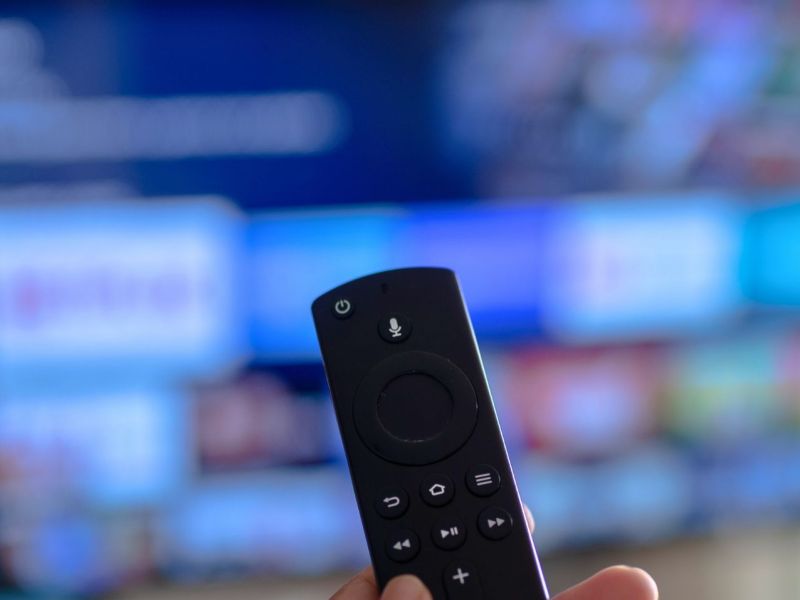 Person hält eine Amazon Fire TV-Fernbedienung auf einem Fernseher gerichtet.