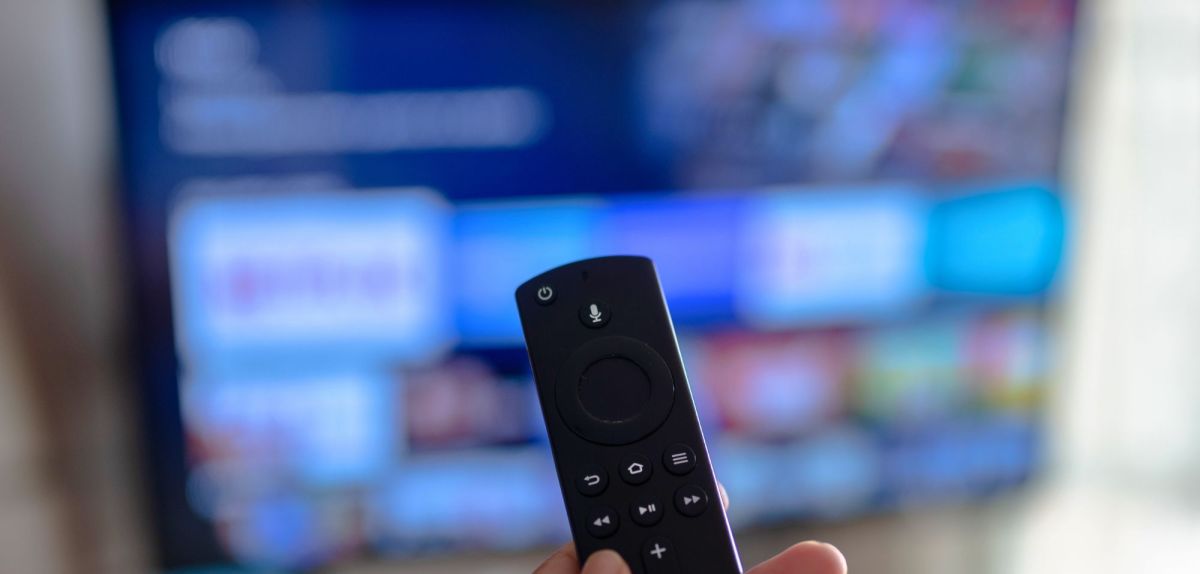 Person hält eine Amazon Fire TV-Fernbedienung auf einem Fernseher gerichtet.