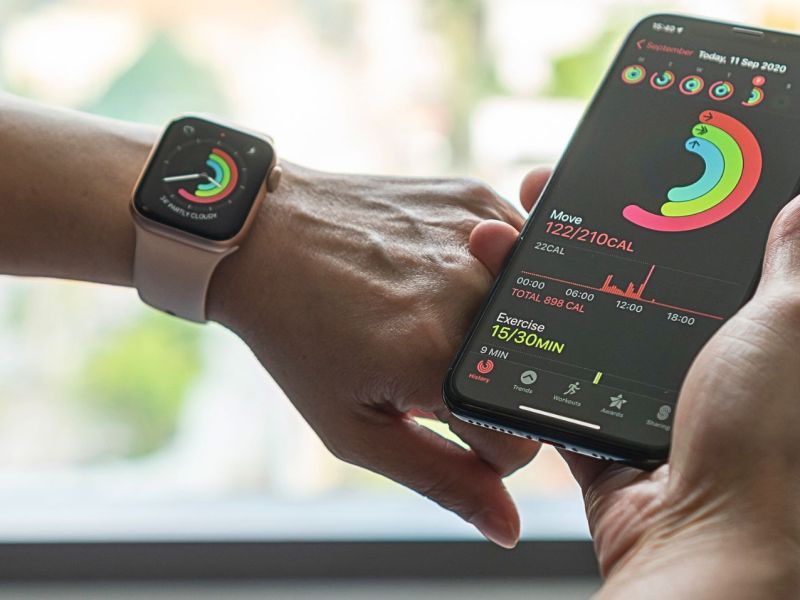 Person trägt eine Apple Watch am Handgelenk. In deren Hand hält sie ein Smartphone.