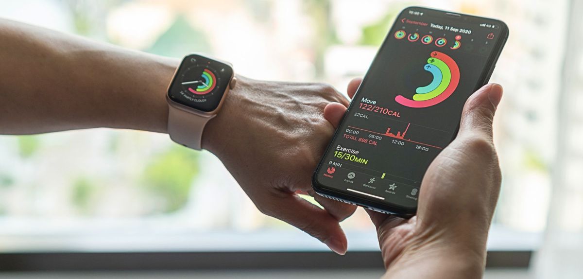 Person trägt eine Apple Watch am Handgelenk. In deren Hand hält sie ein Smartphone.