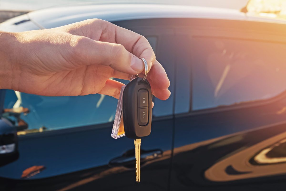 Person hält einen Autoschlüssel. Im Hintergrund ist ein Auto zu sehen.
