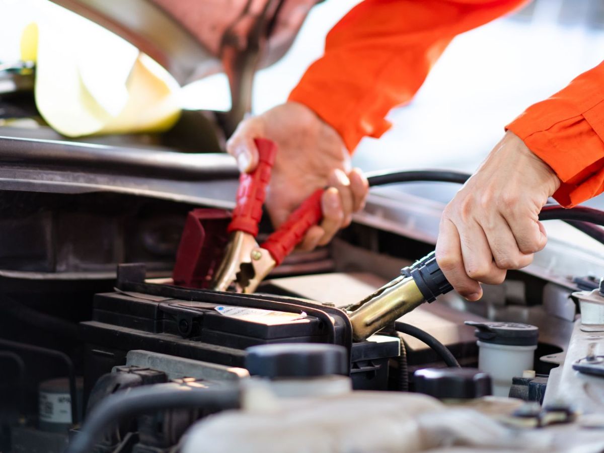 Person schließt zwei Klemmen an eine Autobatterie an.
