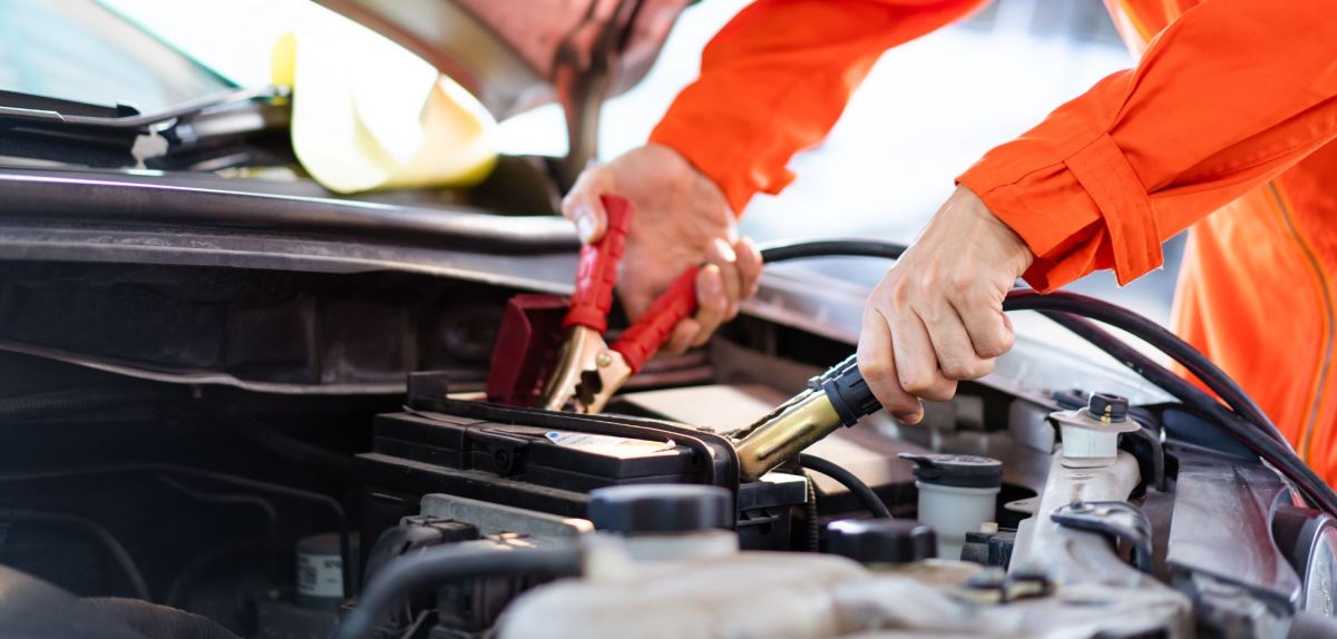 Person schließt zwei Klemmen an eine Autobatterie an.