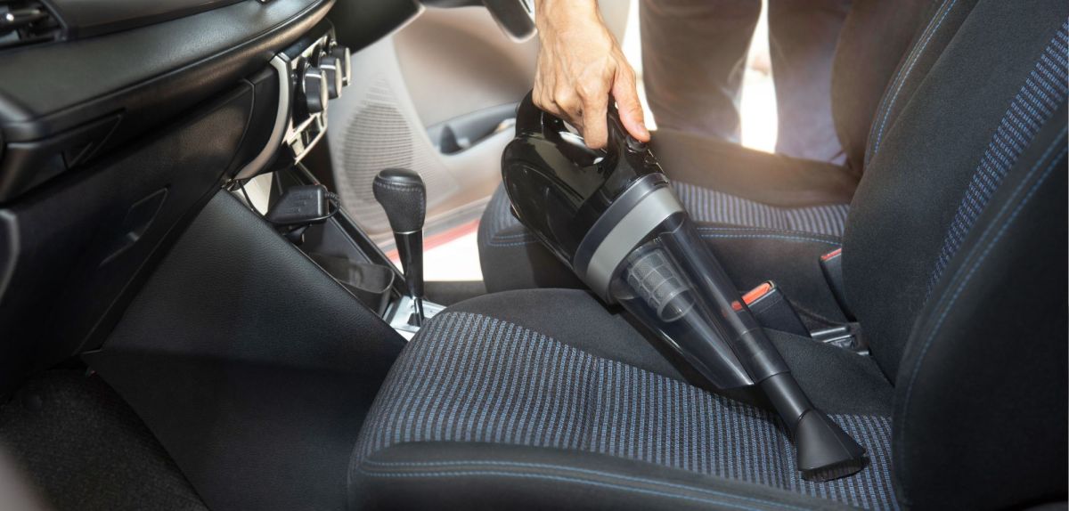 Person reinigt mit einem Akku-Handstaubsauger ein Auto. (Symbolbild)