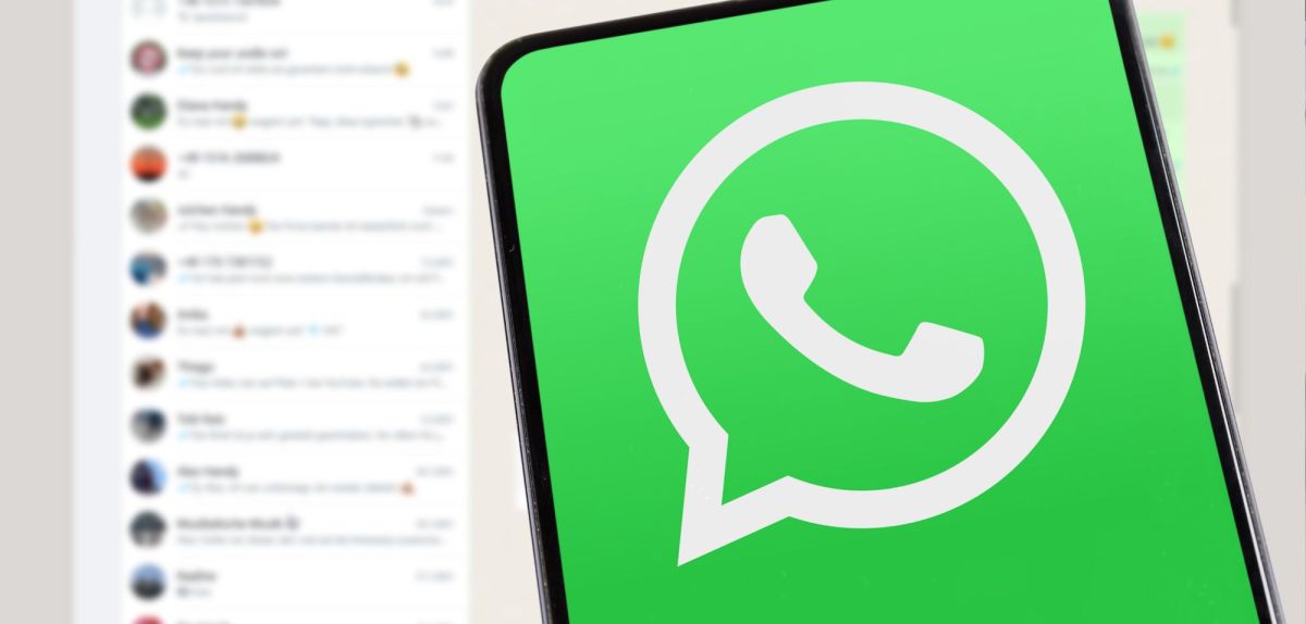 WhatsApp-Logo auf einem Smartphone. Im Hintergrund ist ein Bild zu sehen, auf dem WhatsApp geöffnet ist.