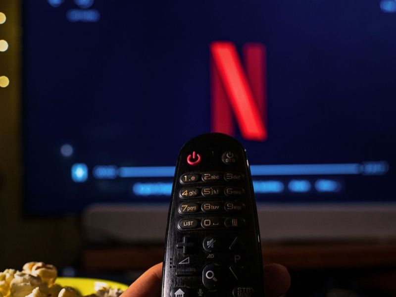 Netflix_Symbol wird auf einem Fernseher angezeigt. Auf den Fernseher ist eine Fernbedienung gerichtet.