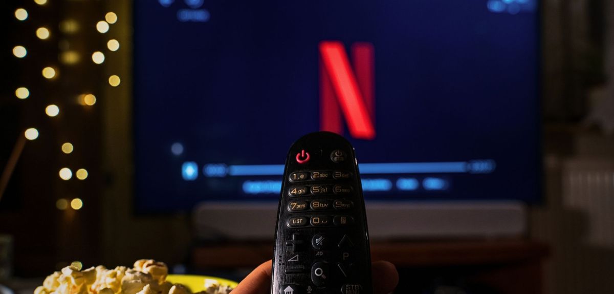 Netflix_Symbol wird auf einem Fernseher angezeigt. Auf den Fernseher ist eine Fernbedienung gerichtet.