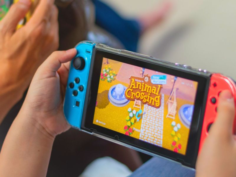 Person hält eine Nintendo Switch in der Hand. Auf der Konsole wird Animal Crossing angezeigt.