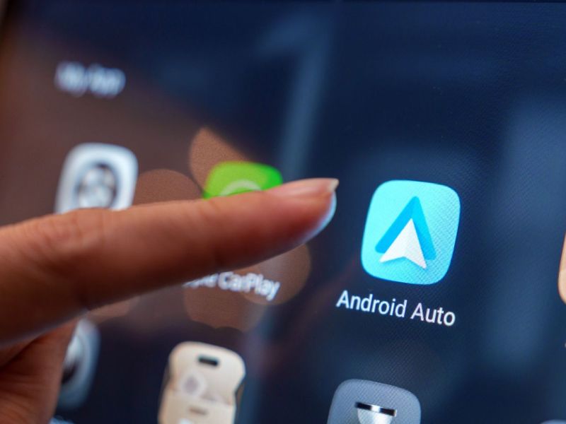 Person zeigt mit einem Finger auf Android Auto-App auf einem Display.