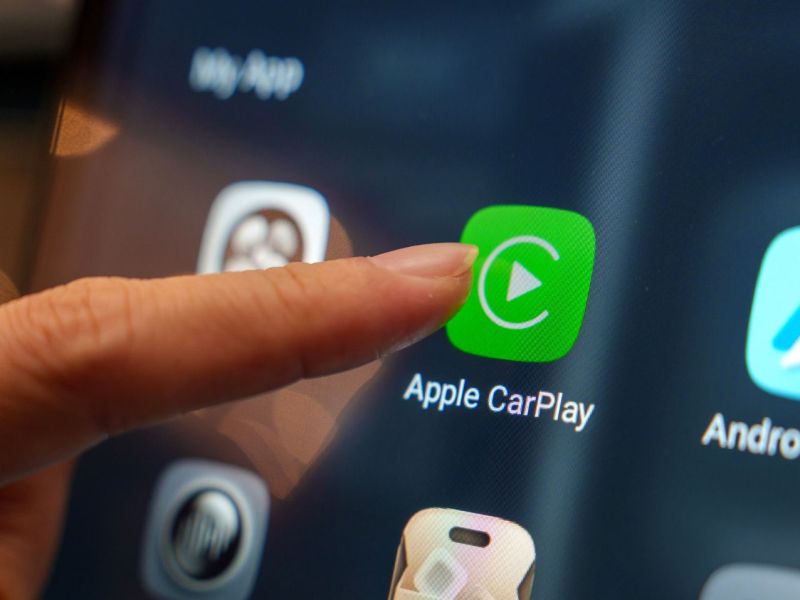Person tippt mit dem Zeigefinger auf die Apple Carplay-App auf einem Display.