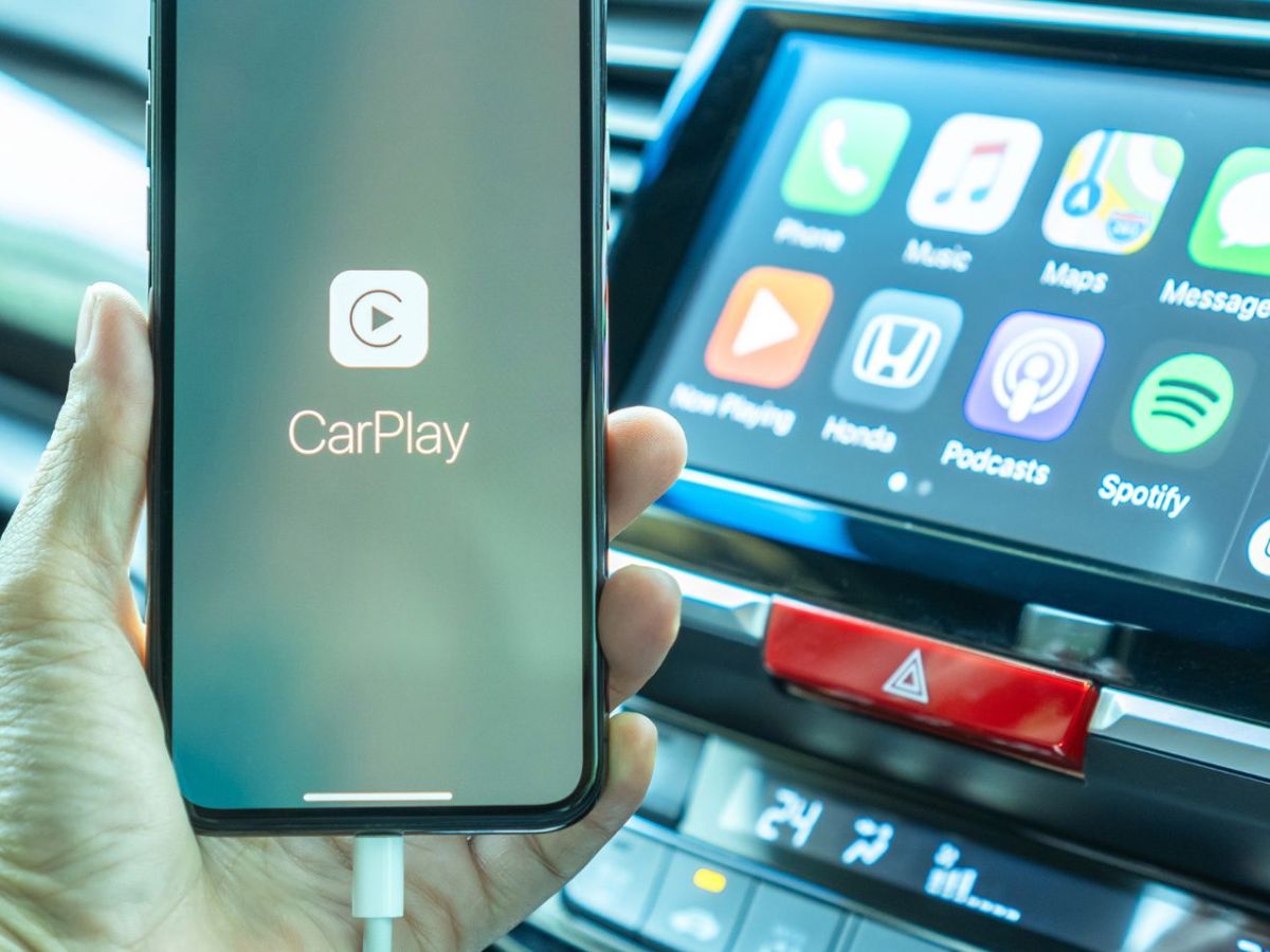Person hält ein Handy in der Hand, das mit einem Auto verbunden ist. Auf dem Display ist das Logo von Apple Carplay zu sehen.