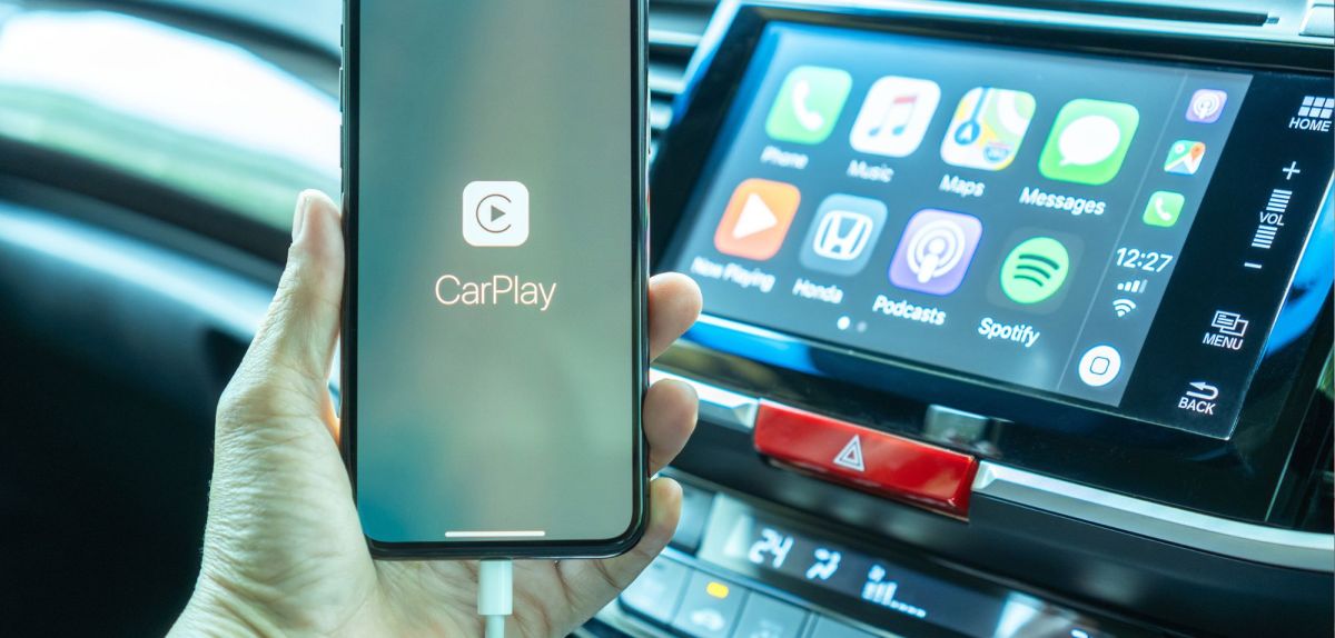 Person hält ein Handy in der Hand, das mit einem Auto verbunden ist. Auf dem Display ist das Logo von Apple Carplay zu sehen.