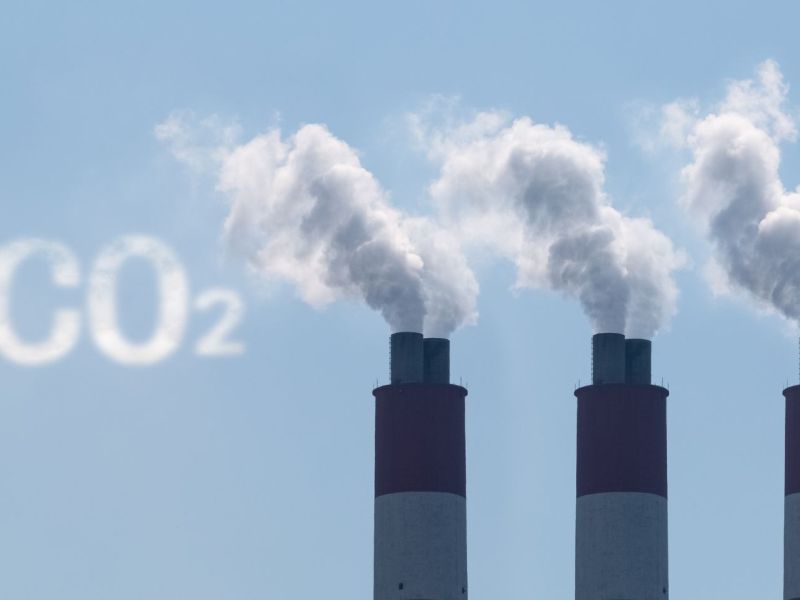 Drei Industrieschornsteine, aus denen Rauch kommt. Daneben steht in der Farbe des Rauchs CO2.