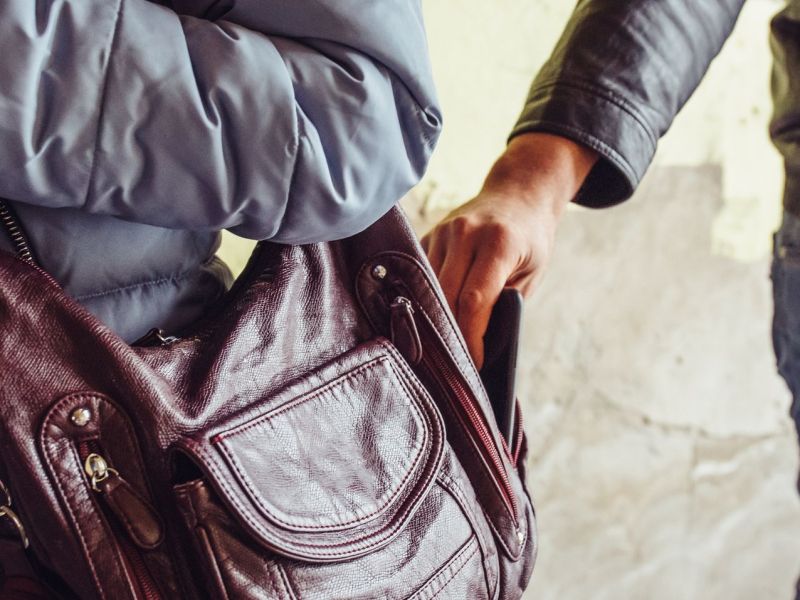 Person klaut ein Handy aus einer Tasche.
