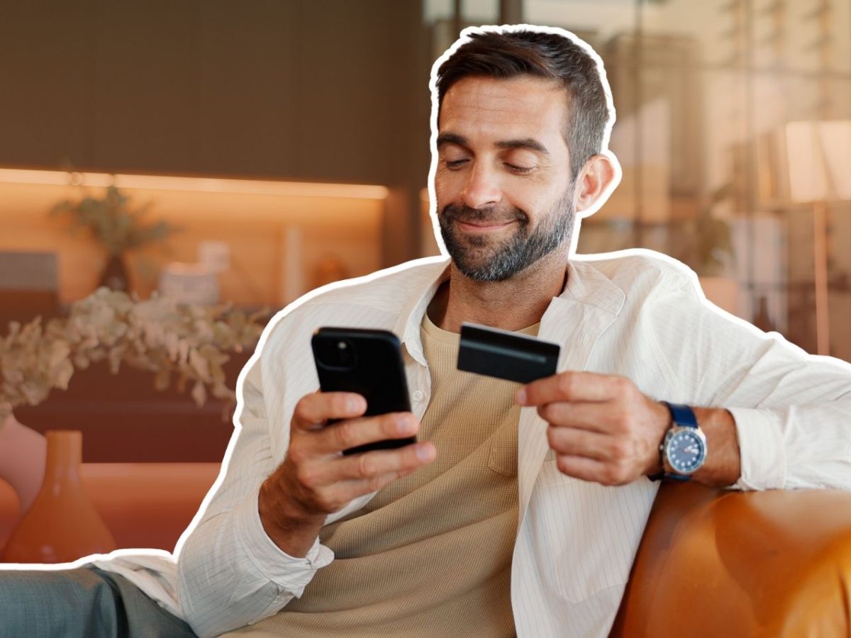 Mann mit Smartphone und Kreditkarte in der Hand auf einem Sessel.