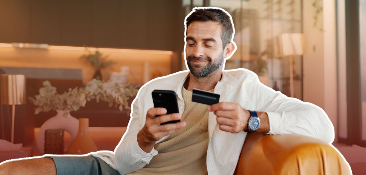 Mann mit Smartphone und Kreditkarte in der Hand auf einem Sessel.