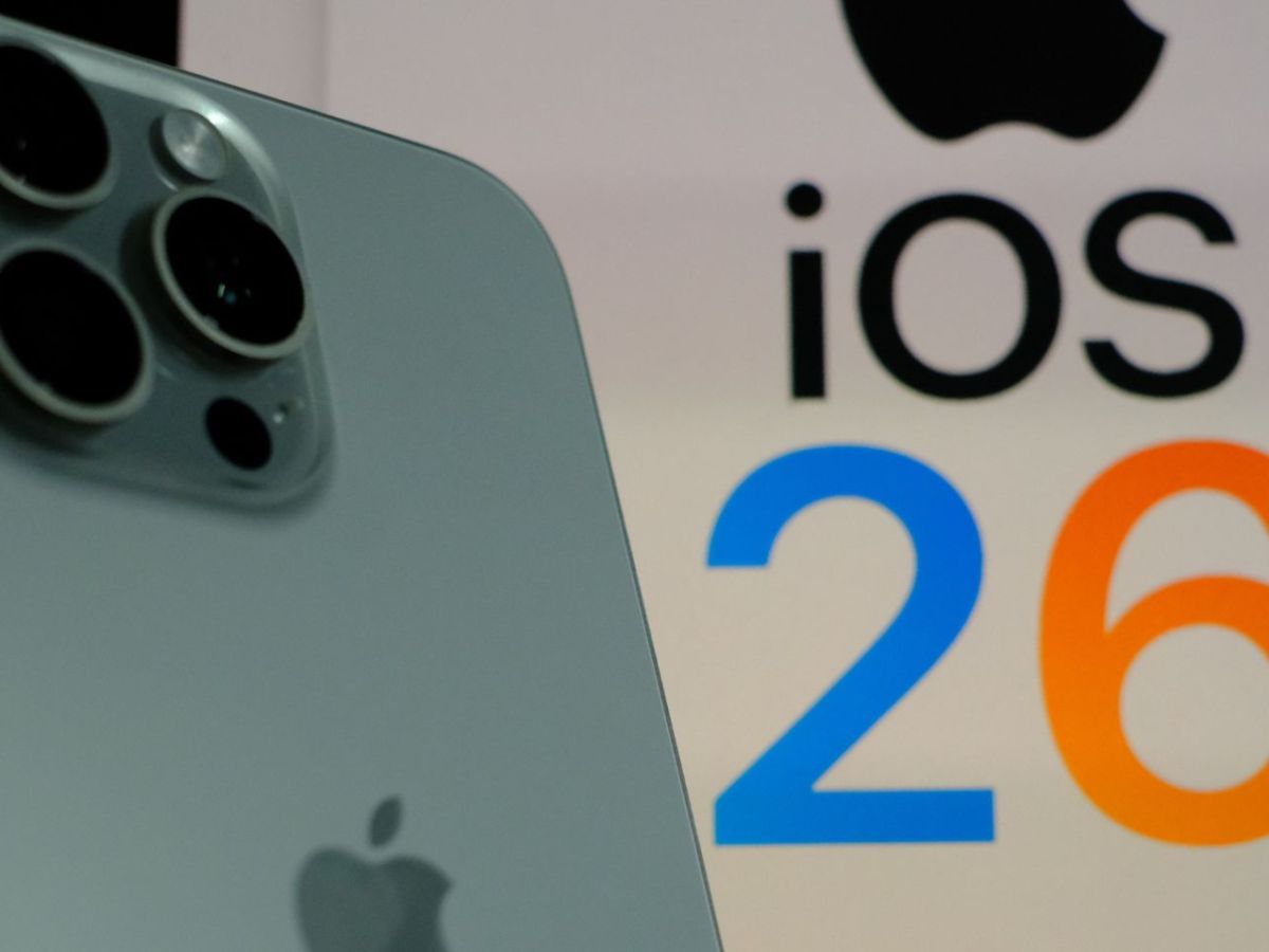 Ein iPhone und im Hintergrund steht iOS 26.