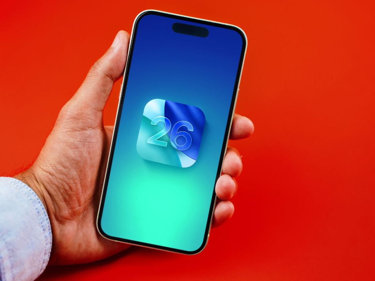 Person hält ein iPhone in der Hand, auf dem Display ist das iOS 26-Logo zu sehen.