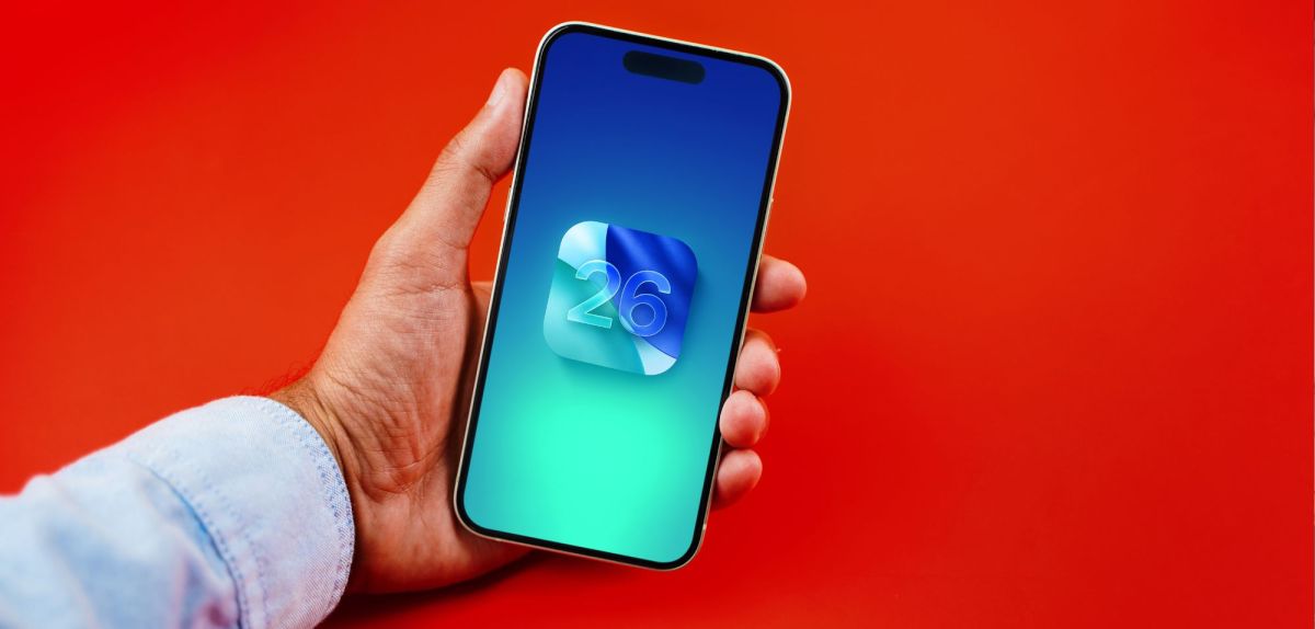 Person hält ein iPhone in der Hand, auf dem Display ist das iOS 26-Logo zu sehen.
