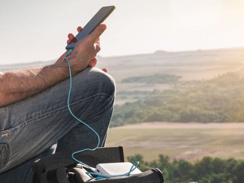 Person lädt Handy im Freien mit einer Powerbank auf.