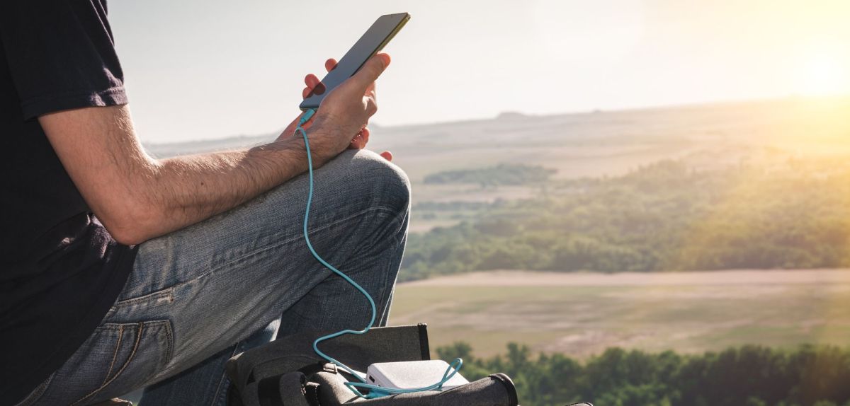 Person lädt Handy im Freien mit einer Powerbank auf.