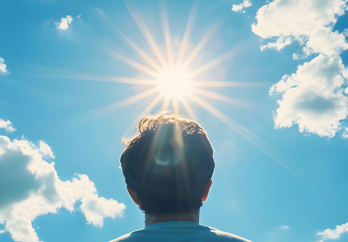 Mensch vor blauem Himmel mit Sonnenstrahlen.