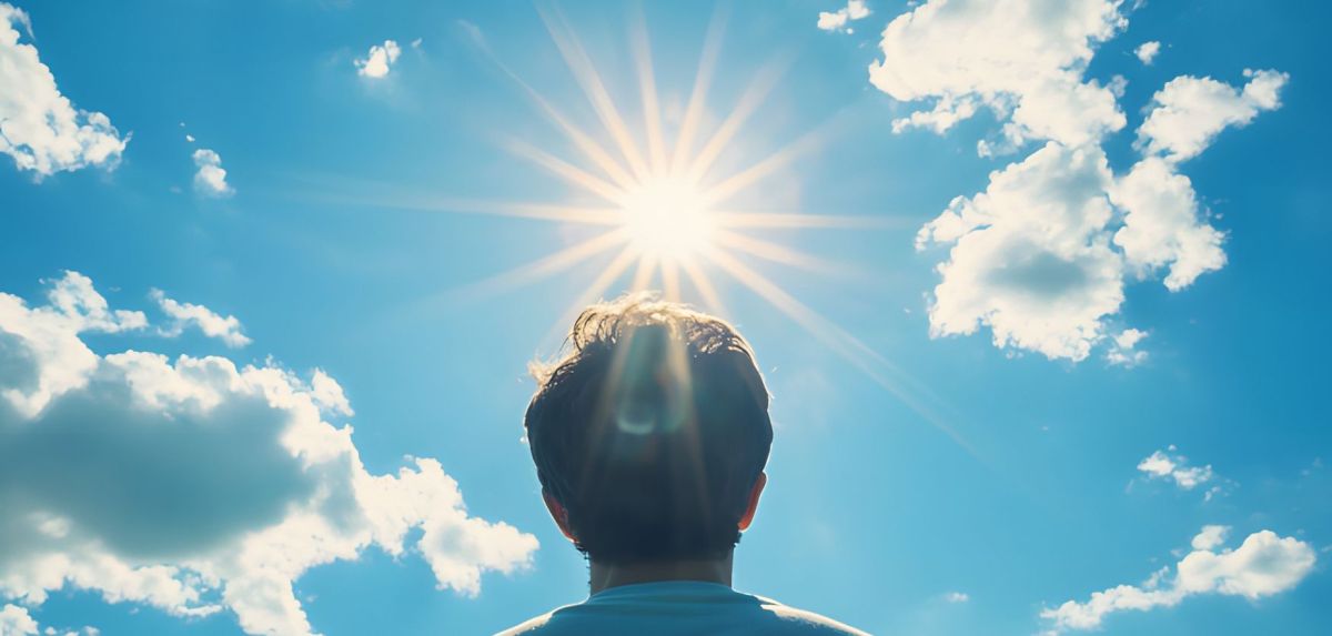 Mensch vor blauem Himmel mit Sonnenstrahlen.