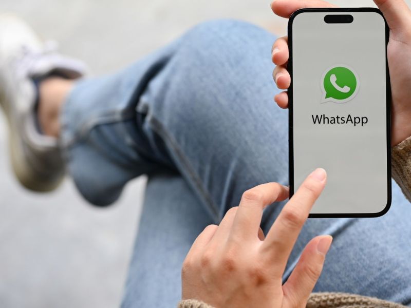 Person hält Handy mit WhatsApp darauf hoch.