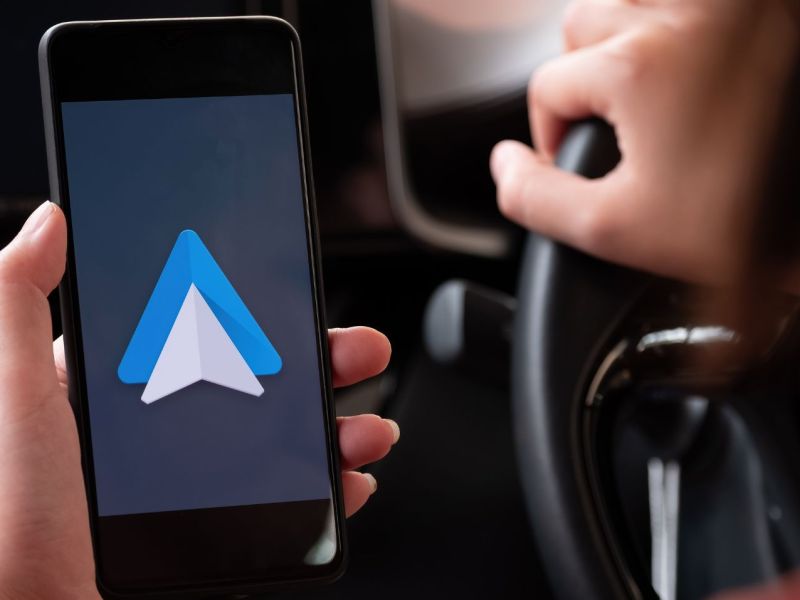 Auf einem Handy wird Android Auto angezeigt. Im Hintergrund ist der Innenraum eines Fahrzeugs zu sehen.