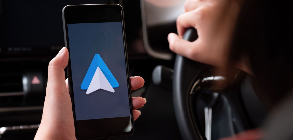 Auf einem Handy wird Android Auto angezeigt. Im Hintergrund ist der Innenraum eines Fahrzeugs zu sehen.
