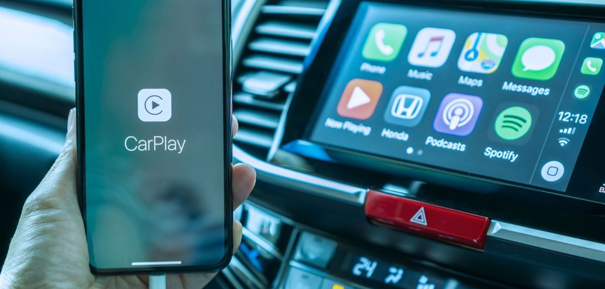 Ein Handy auf dem Apple CarPlay gestartet wird und im Hintergrund der Innenraum eines Autos.