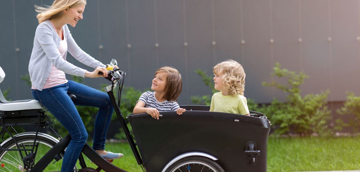 Mutter fährt auf E-Bike mit Kindern im Lastenbereich.