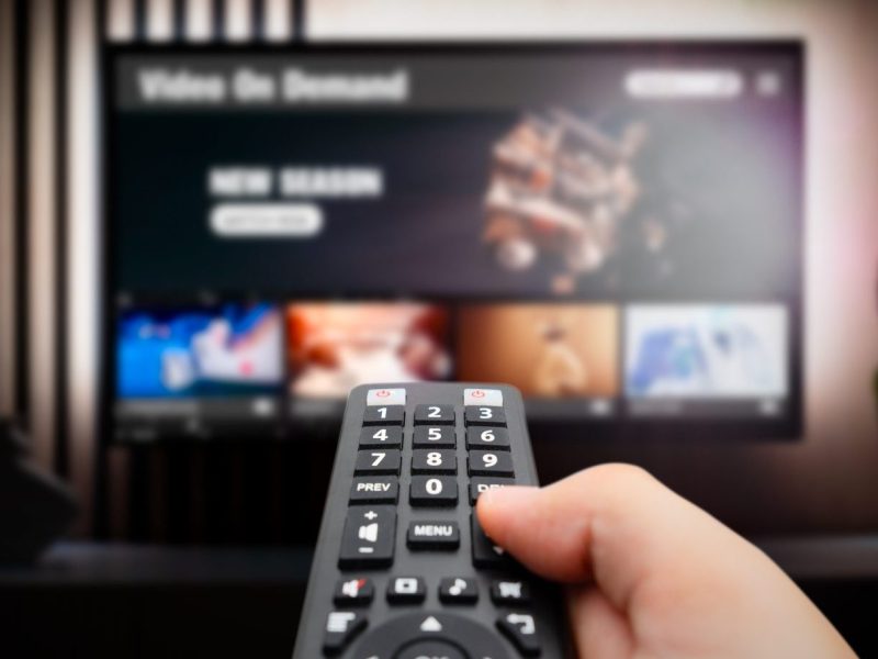 Person hält eine Fernbedienung auf einen Fernseher