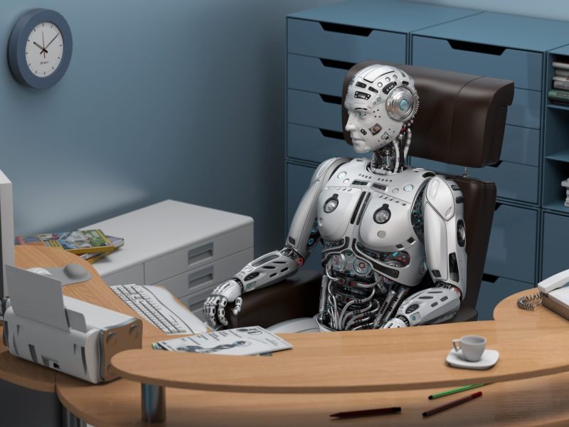 Roboter sitzt am Schreibtisch im Büro