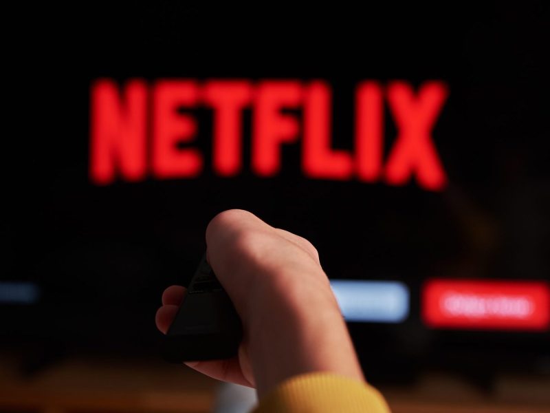 Person hält die Fernbedienung in Richtung Fernseher mit Netflix-Logo