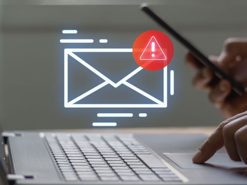 Person hält Smartphone und tippt auf einem Laptop. Ein Email-Icon wird angezeigt.