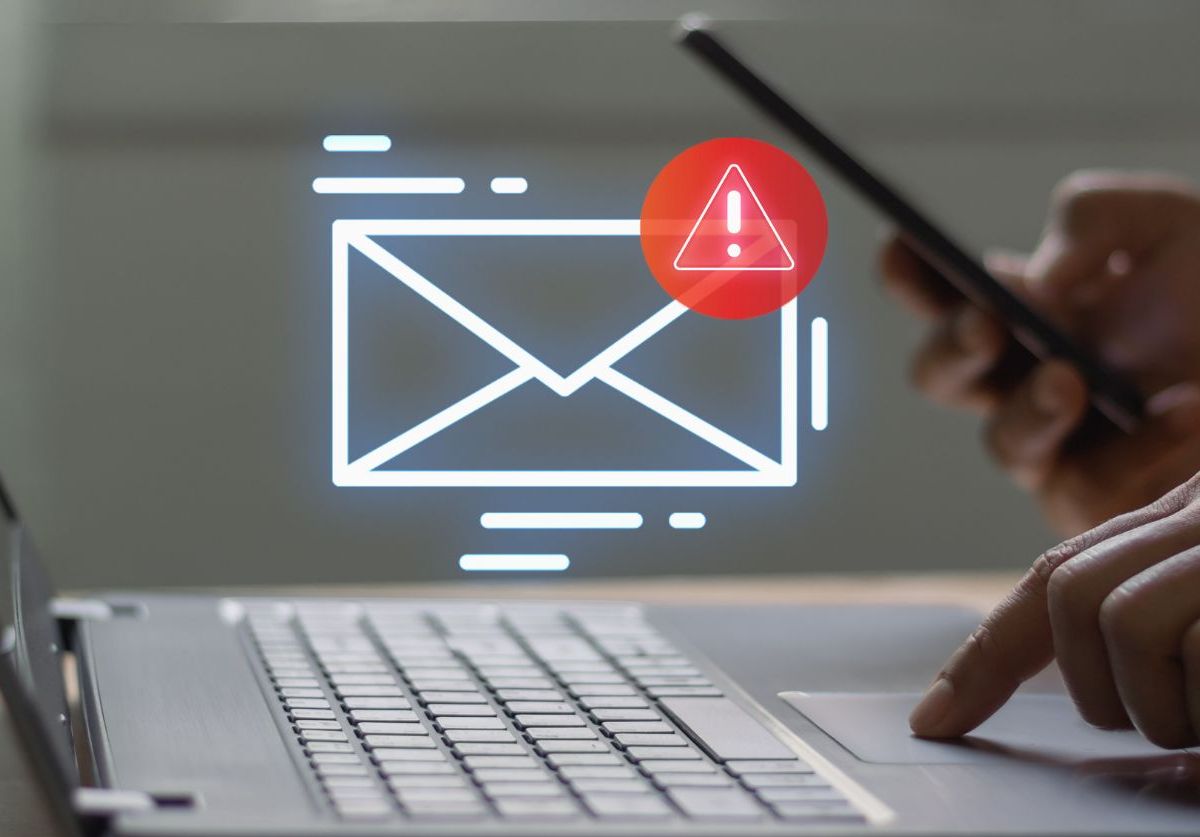 Person hält Smartphone und tippt auf einem Laptop. Ein Email-Icon wird angezeigt.