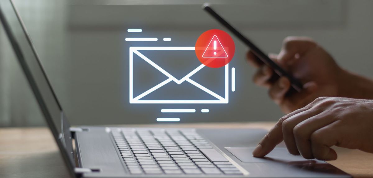 Person hält Smartphone und tippt auf einem Laptop. Ein Email-Icon wird angezeigt.