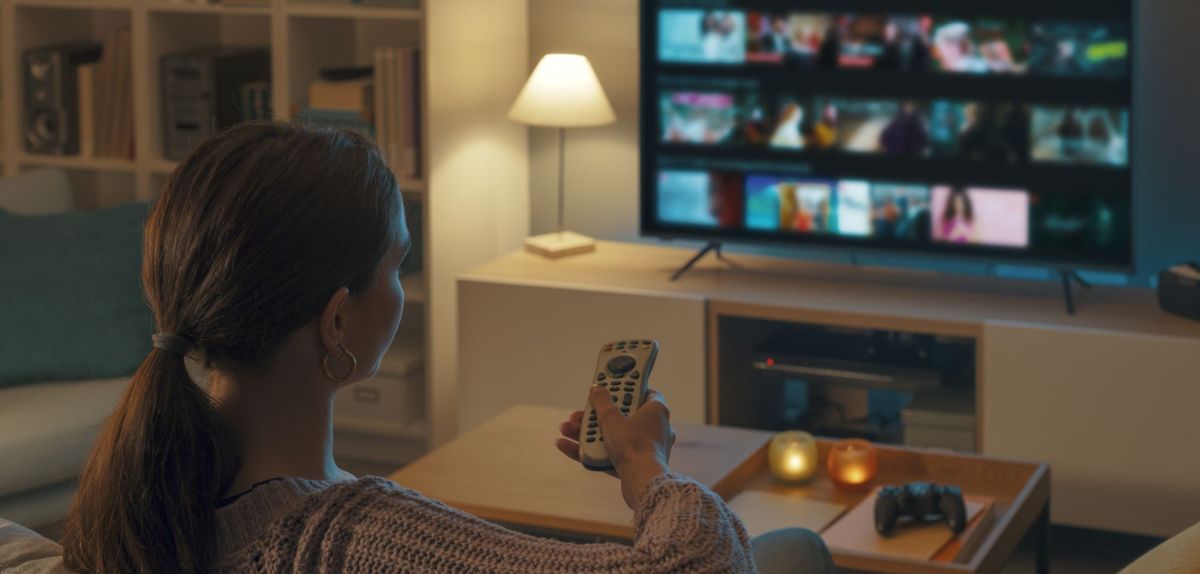 Person sitzt in einem Wohnzimmer vor einem Fernseher.