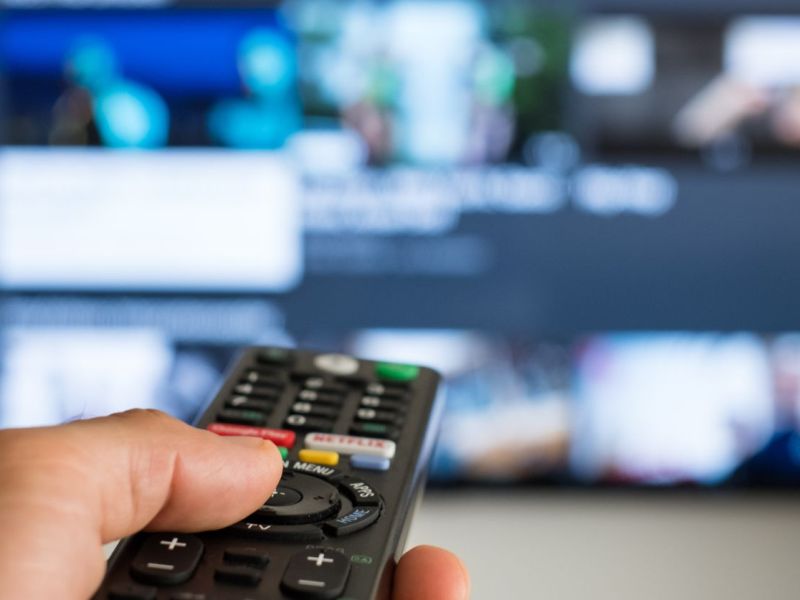 Unbekannte Person richtet Fernbedienung auf einen Fernseher.
