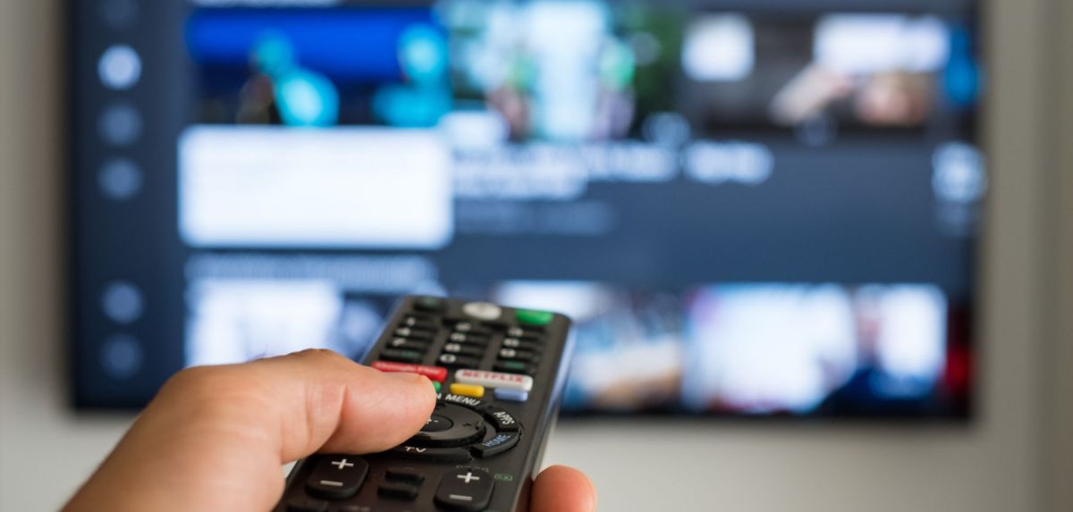 Unbekannte Person richtet Fernbedienung auf einen Fernseher.