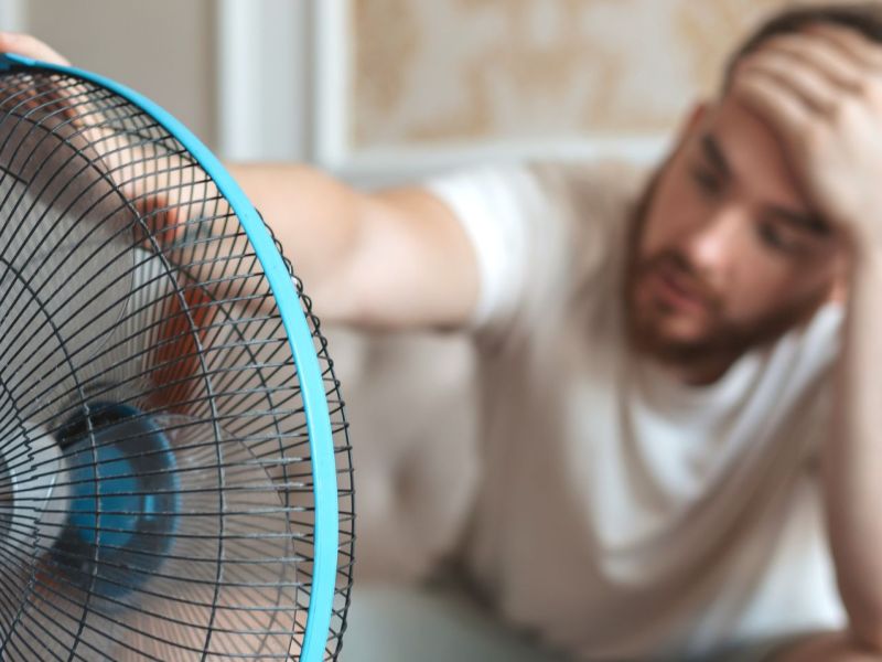 Mann sitzt vor einem Ventilator.