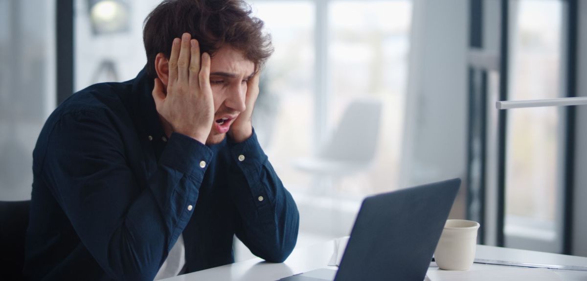Person sitzt vor einem Laptop und schlägt die Hände vor dem Gesicht zusammen.