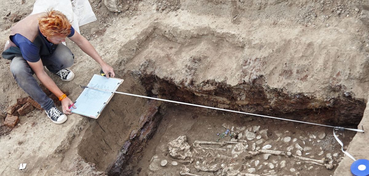 Person kniet vor einer Grube, in der sich mehrere Knochen befinden.