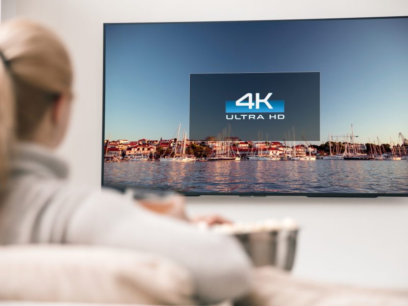 Frau sitzt vor Fernseher an einer Wand